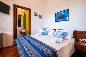 Een hotelkamer met een bed, een badkamer, een televisie en een ingelijst schilderij aan de muur.