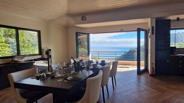 Un coin repas avec vue sur l’océan, une cuisine également avec vue, et une table à manger dressée avec des assiettes et des verres.