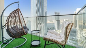 A balcony with a hanging chair, a cushioned chair, and a small table. - Silkhaus The Grand (Dubai)