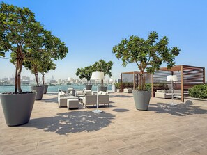 An outdoor seating area with potted plants, lounge chairs, and a view of the city skyline. - Silkhaus The Grand (Dubai)