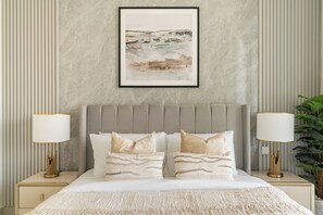 Ein Schlafzimmer mit einem Bett, zwei Nachttischlampen, einem gerahmten Kunstwerk an der Wand und einer Zimmerpflanze.