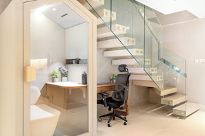 A modern office space with a glass staircase, a desk, office chair, and a plant. - Silkhaus Azure (Abu Dhabi)