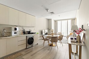 Een moderne keuken met een ingebouwde wasmachine, een eethoek met een ronde tafel en een uitzicht op een hoog gebouw door grote ramen.