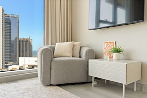 Een moderne woonkamer met een grijze bank, een witte bijzettafel en een groot raam met uitzicht op de stad.