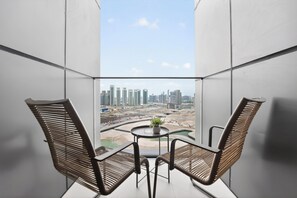A balcony with two wicker chairs, a small table with a plant, and a view of a cityscape with high-rise buildings. - Silkhaus Radiant Bay (Abu Dhabi)