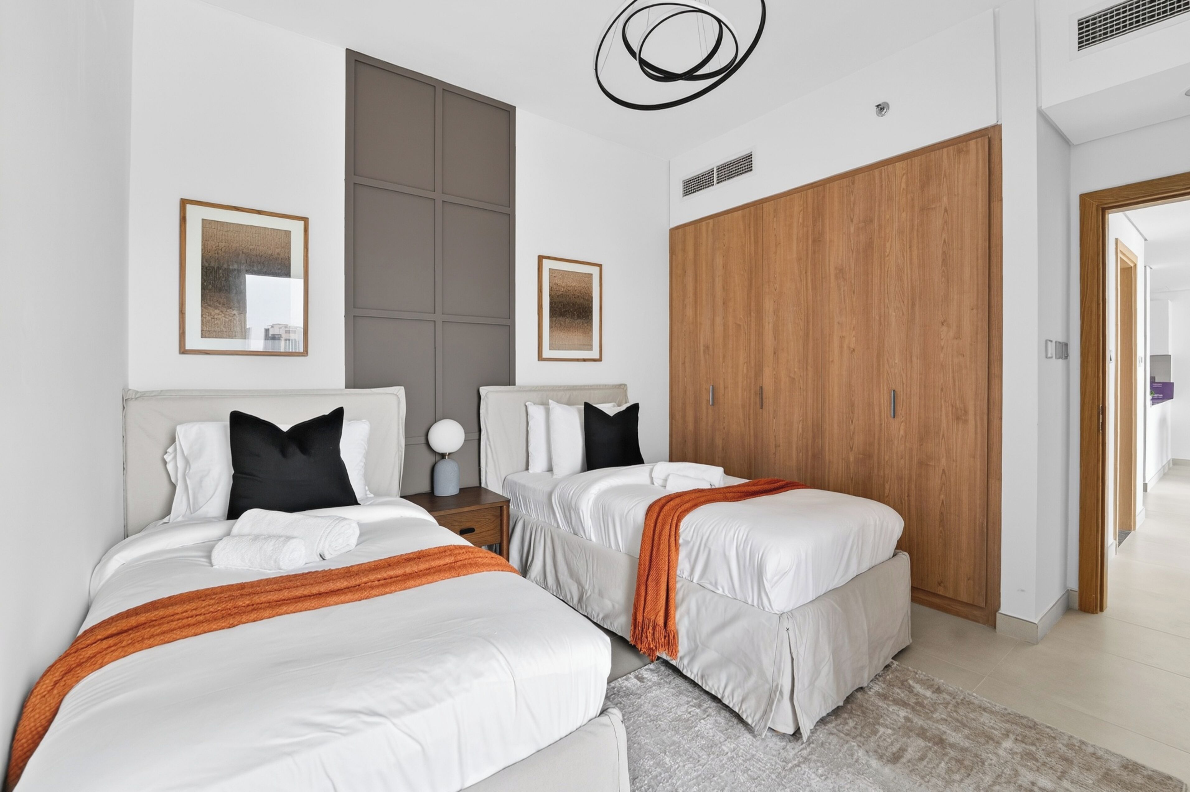 A modern hotel room with two beds, a large wardrobe, and a view of the hallway.