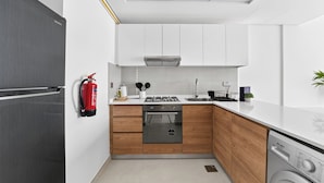 Une cuisine compacte avec des meubles blancs, un réfrigérateur en acier inoxydable, une cuisinière à gaz et un four encastré.