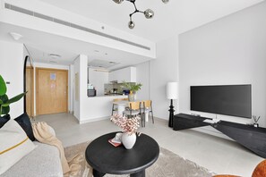 Ein modernes Wohnzimmer mit Flachbildfernseher, einer Essecke mit Tisch und Stühlen sowie einer Küche im Hintergrund.