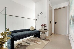 Een moderne woonkamer met een donkerblauwe bank, een rond bijzettafeltje met decoratieve items, een vloerlamp en een grote spiegel aan de muur.