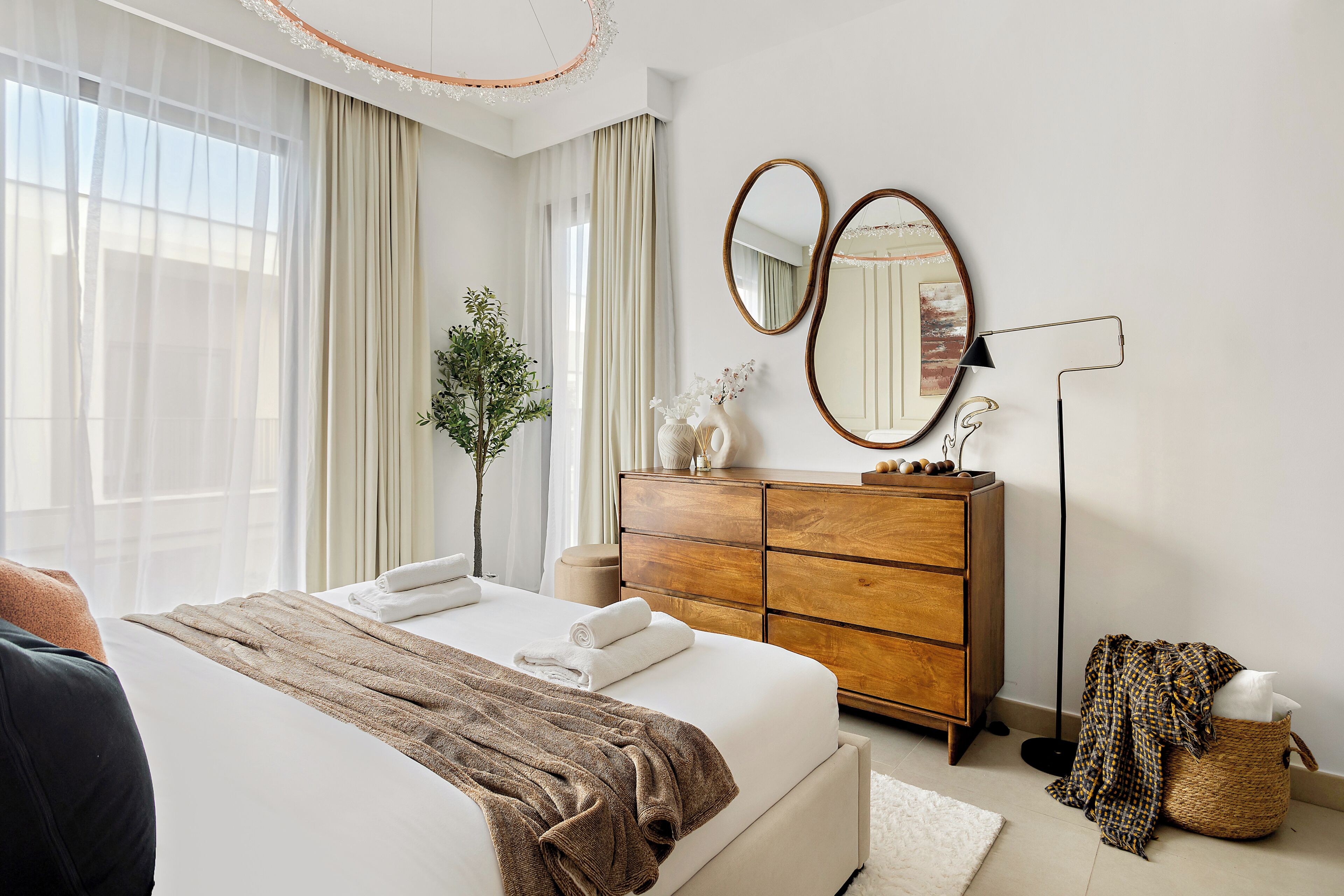 A modern bedroom with a large bed, wooden dresser, and two mirrors.