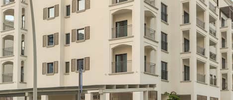 Un immeuble résidentiel à plusieurs étages, doté de balcons, d’un espace de stationnement et surplombant un ciel dégagé.