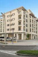Un edificio residencial de varios pisos con balcones, un estacionamiento y cielo despejado.