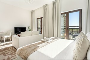 Habitación de hotel con cama, sofá, televisión y balcón con vistas.