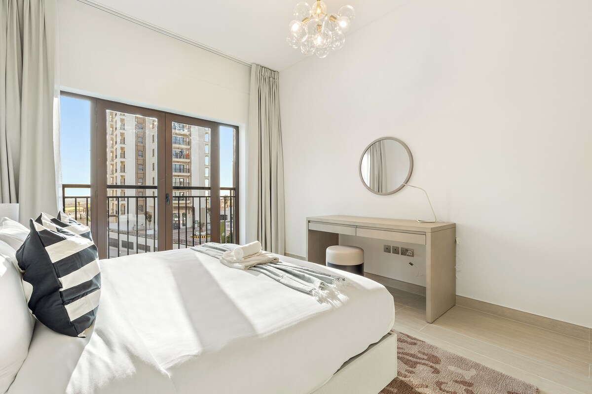 Habitación de hotel con una cama grande, un escritorio, un espejo y vistas a un edificio a través de la ventana.