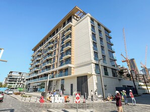 Ein mehrstöckiges Gebäude mit Balkonen, ein Baugrundstück davor und ein klarer Himmel.