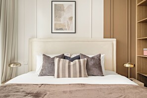 Un lit avec une tête de lit blanche, plusieurs oreillers et une couverture beige.