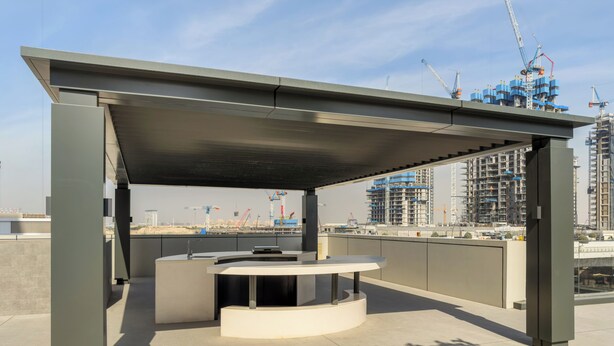 Un espacio al aire libre con mesa y sillas, una sección cubierta y vista a una obra en construcción al fondo.