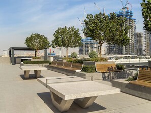 Een terras met banken en plantenbakken, omgeven door bomen en uitzicht op een bouwplaats met kranen.