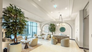 Un vestíbulo amplio con una palmera grande en maceta, asientos cómodos, una recepción y un ventanal con vistas.