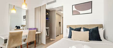 Une chambre d’hôtel avec un lit, un bureau et une chaise. Il y a un miroir au mur et un cadre photo.