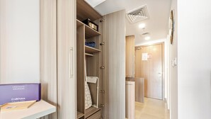 A hotel room with a wardrobe, a desk with a purple folder, and a shower area. - Silkhaus Leonardo Residences (Abu Dhabi)