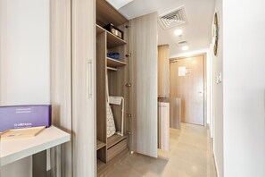 Une chambre d’hôtel avec un placard, un bureau sur lequel se trouve un classeur violet, et un espace douche.