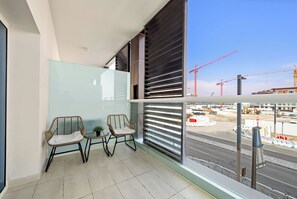 Een balkon met twee rieten stoelen, een tafeltje en een glazen balustrade.