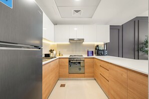 A modern kitchen with stainless steel appliances, wooden cabinets, and a white countertop. - Silkhaus Radiant Heights (Abu Dhabi)