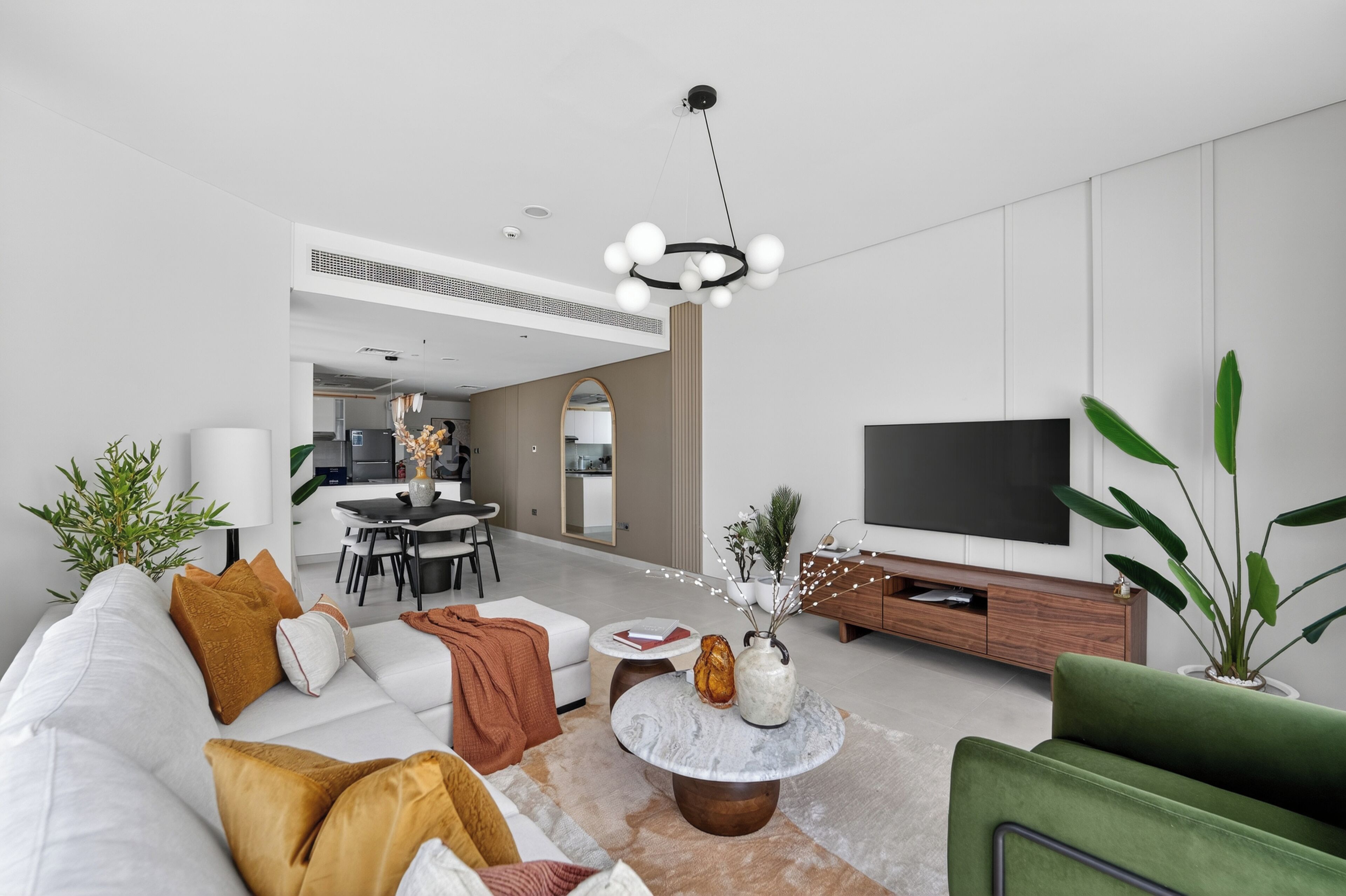 Een moderne woonkamer met een bank, salontafel en een televisie. Achterin is een eethoek.