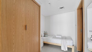Une chambre à coucher avec une armoire en bois, un lit avec un matelas et des oreillers blancs, une table de chevet et une petite lampe de chevet.