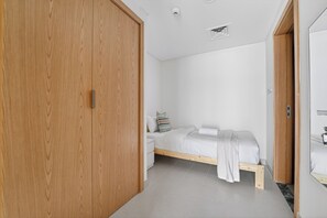 Ein Schlafzimmer mit Holzschrank, einem Bett mit weißer Matratze und Kissen, einem Nachttisch und einer kleinen Nachttischlampe.