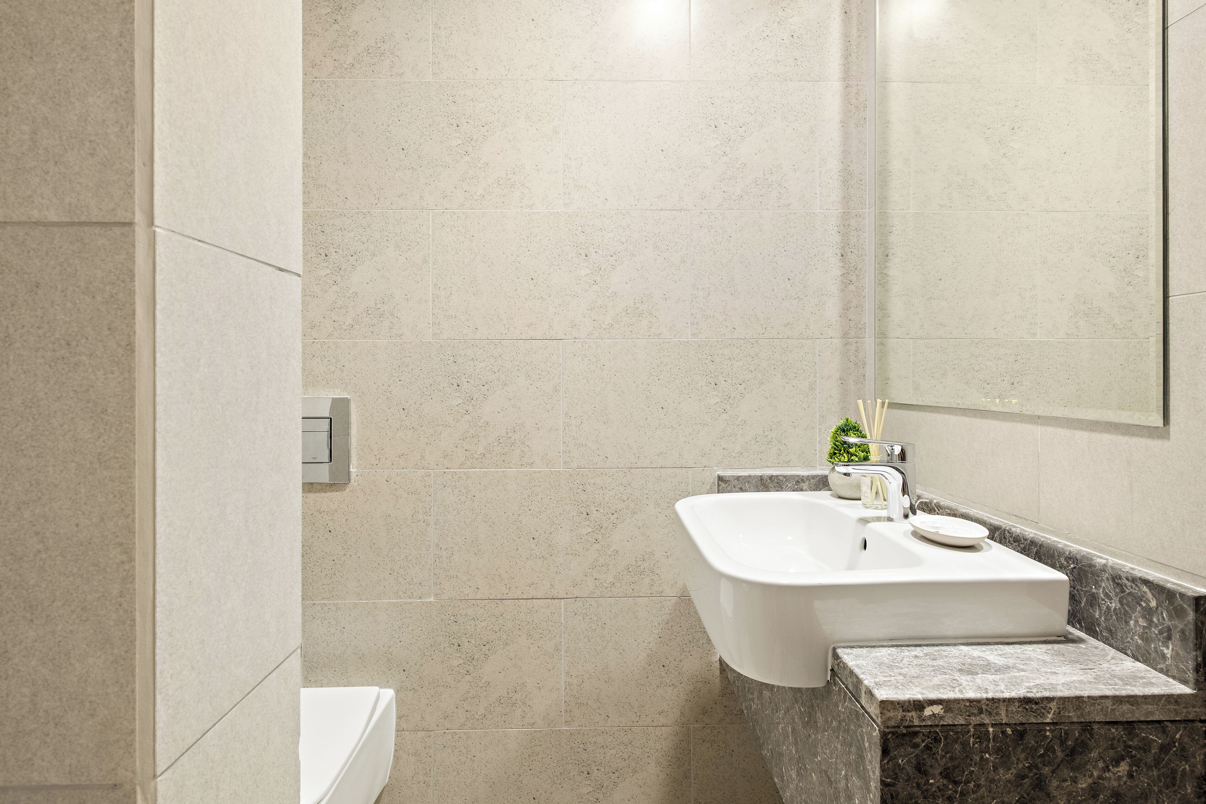 A modern bathroom with a white sink, a mirror, and a marble countertop.