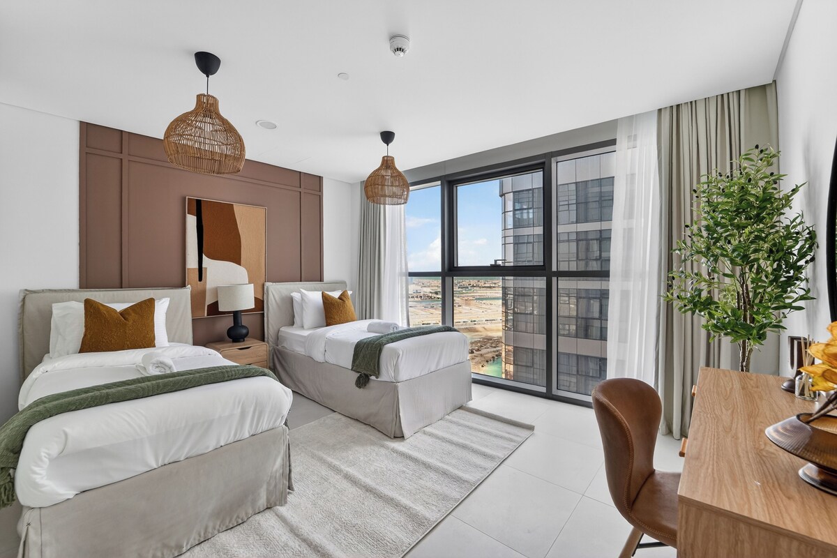A modern hotel room with two beds, a desk, and a large window offering a city view.