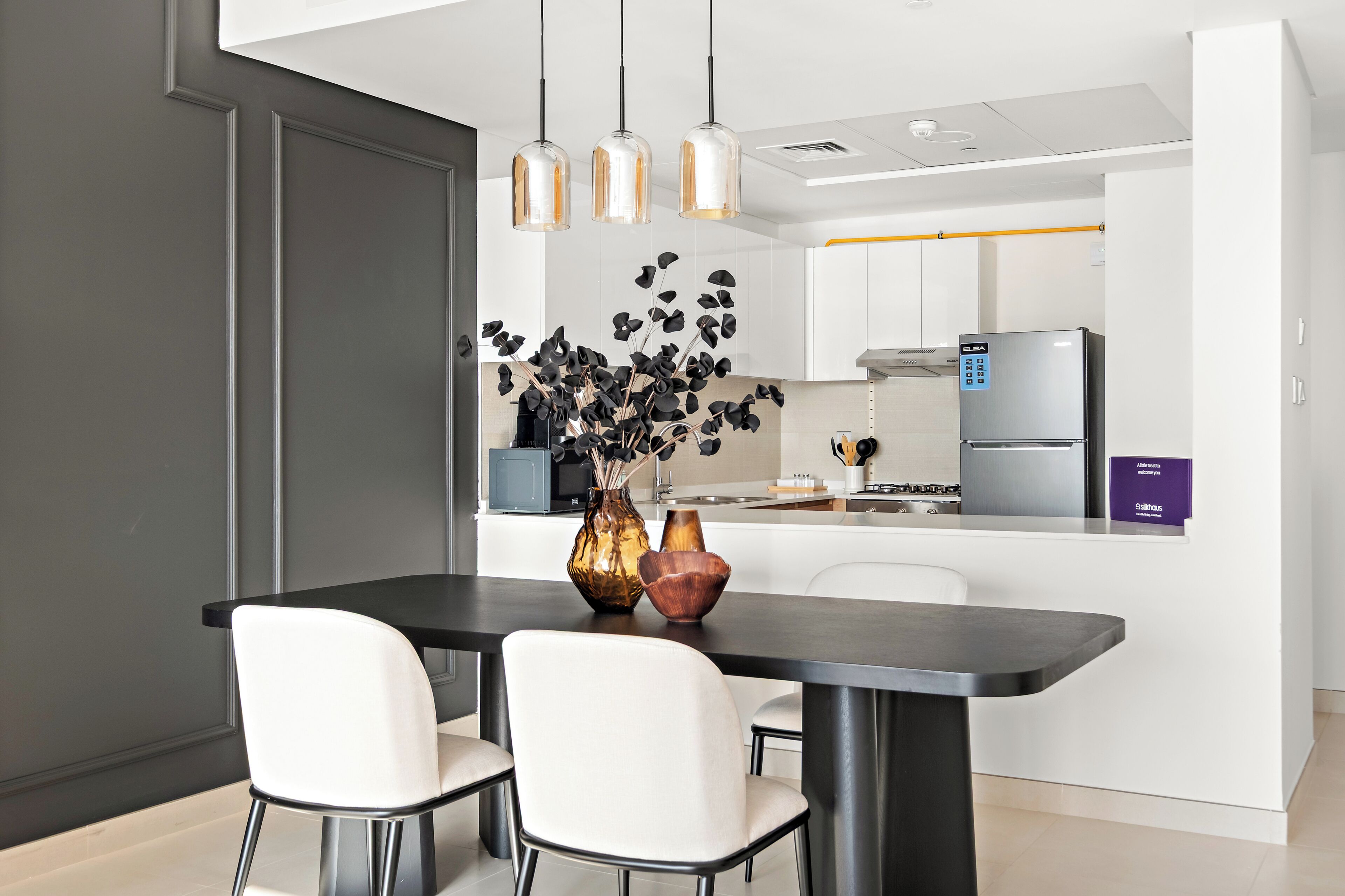 Een moderne keuken met een eethoek, met een zwarte tafel, witte stoelen en een vaas met bloemen.