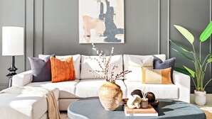 Un salon moderne avec un canapé blanc, des coussins décoratifs, un vase avec des branches et une plante en pot.