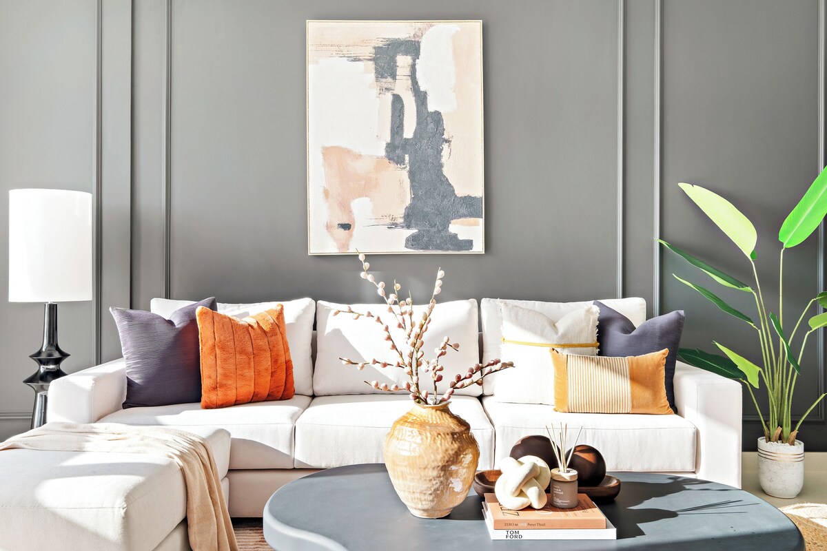Ein modernes Wohnzimmer mit einem weißen Sofa, dekorativen Kissen, einer Vase mit Zweigen und einer Topfpflanze.