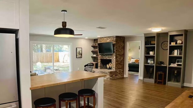 Une cuisine moderne dotée d’un îlot central, de tabourets de bar en bois, d’une cheminée en pierre et d’un téléviseur fixé au mur.