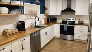 Une cuisine moderne avec des armoires blanches, un plan de travail en bois, des appareils en acier inoxydable et un mur d’accent bleu.