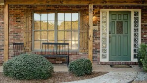 Un bâtiment rustique avec une porte verte, un banc à l’extérieur et une façade en briques.