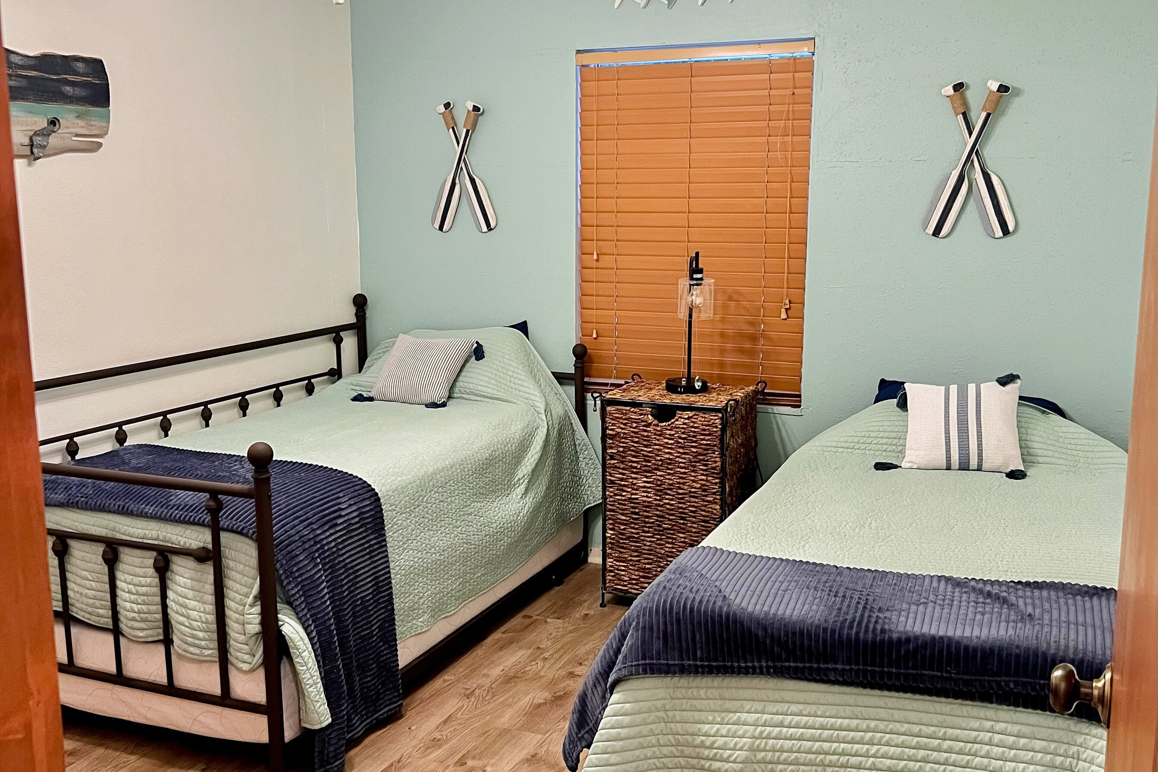 A bedroom with two beds, a wooden floor, and a window with blinds.