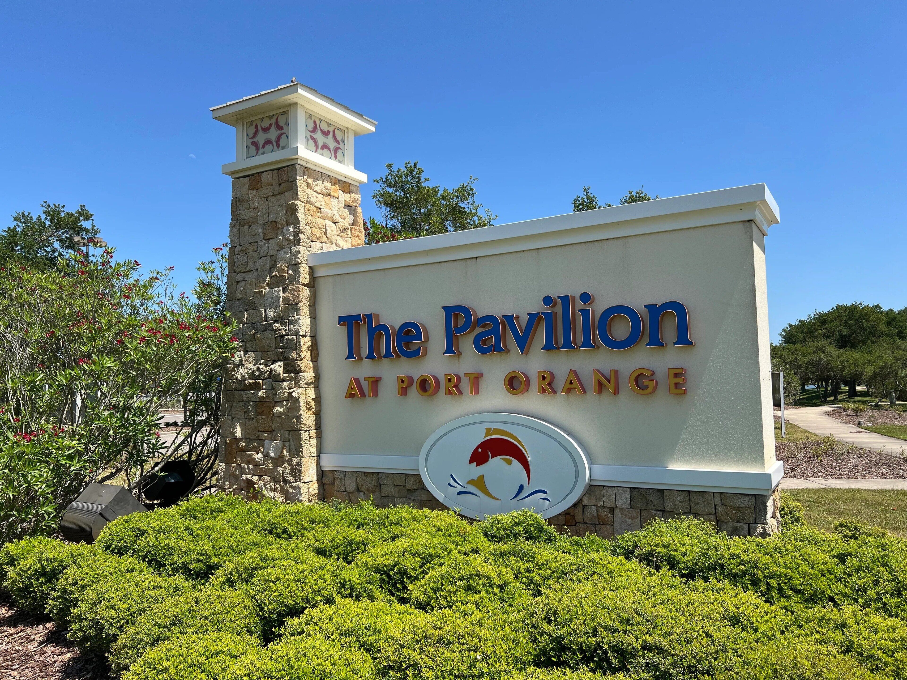 A sign for "The Pavilion at Port Orange" with a stone tower and well-maintained greenery.