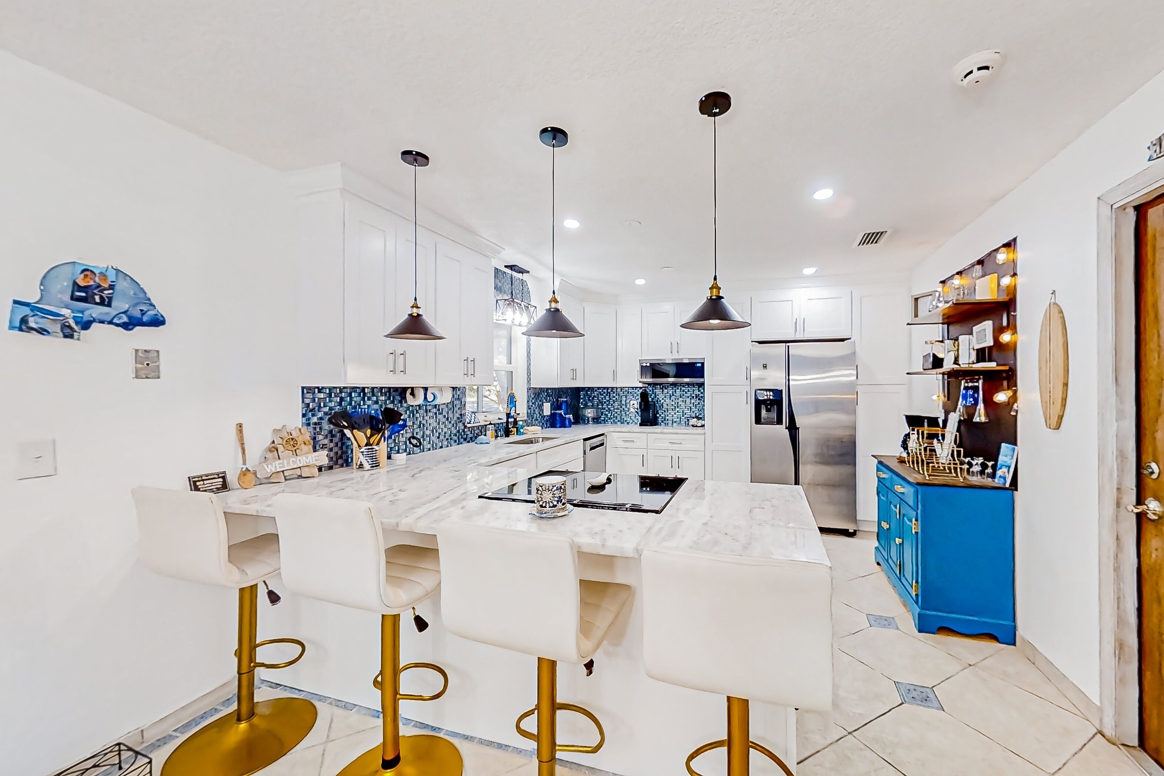 A modern kitchen with white cabinets, a marble island, and gold bar stools.