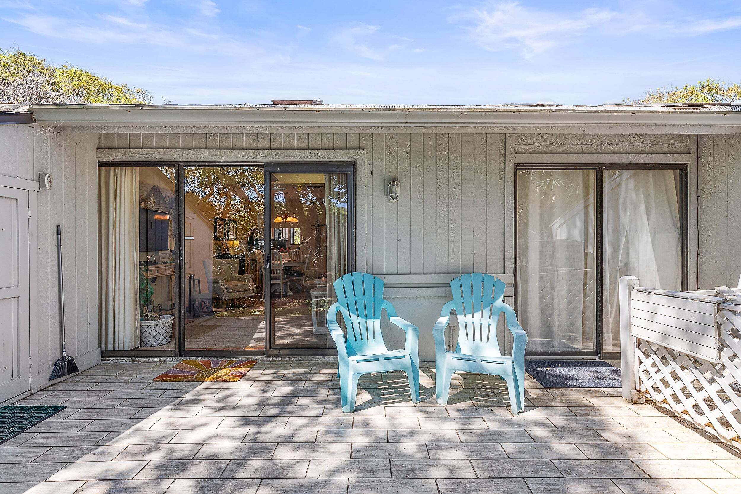 A covered patio with two Adirondack chairs, a sliding glass door, and a white fence.