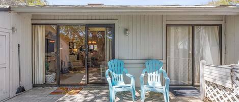 A covered patio with two Adirondack chairs, a sliding glass door, and a white fence.