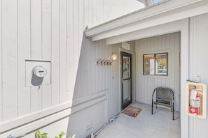 A white building with a door, a chair, a fire extinguisher, and a meter. - NSB 4360 Sea Woods- After Dune Delight (New Smyrna Beach)