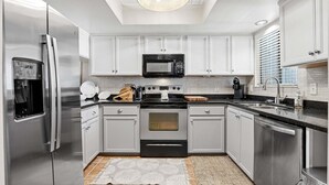 A modern kitchen with stainless steel appliances, white cabinetry, and a patterned rug. - NSB 4360 Sea Woods- After Dune Delight (New Smyrna Beach)