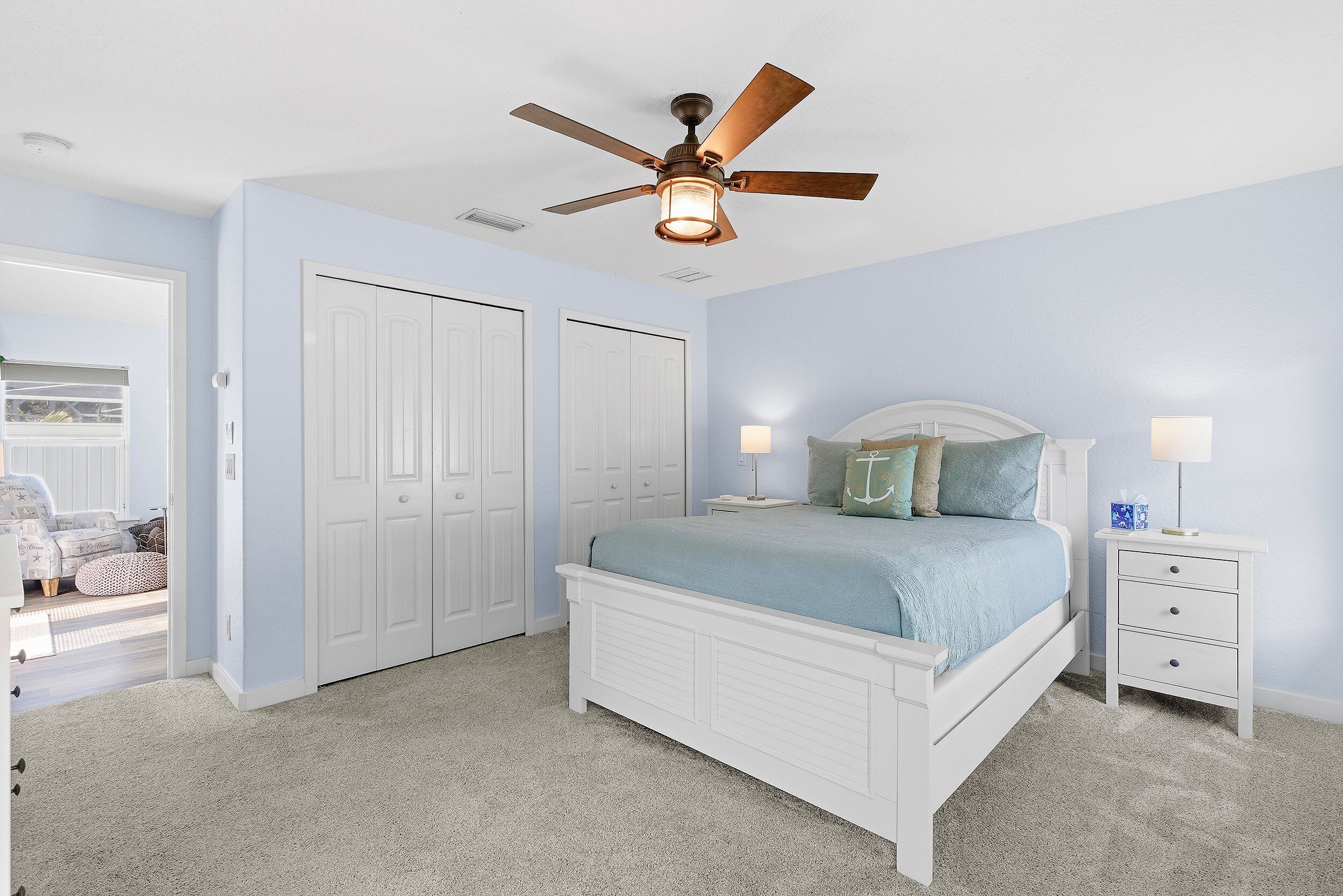 Une chambre à coucher comprenant un lit, des tables de chevet, un ventilateur de plafond et un placard.