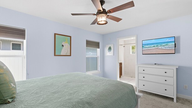 A bedroom with a bed, a ceiling fan, a dresser, and a TV on the wall. - Terrapin Station (Ormond Beach)