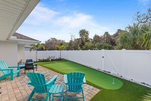 A patio with turquoise Adirondack chairs, a small table, and a putting green. - Terrapin Station (Ormond Beach)