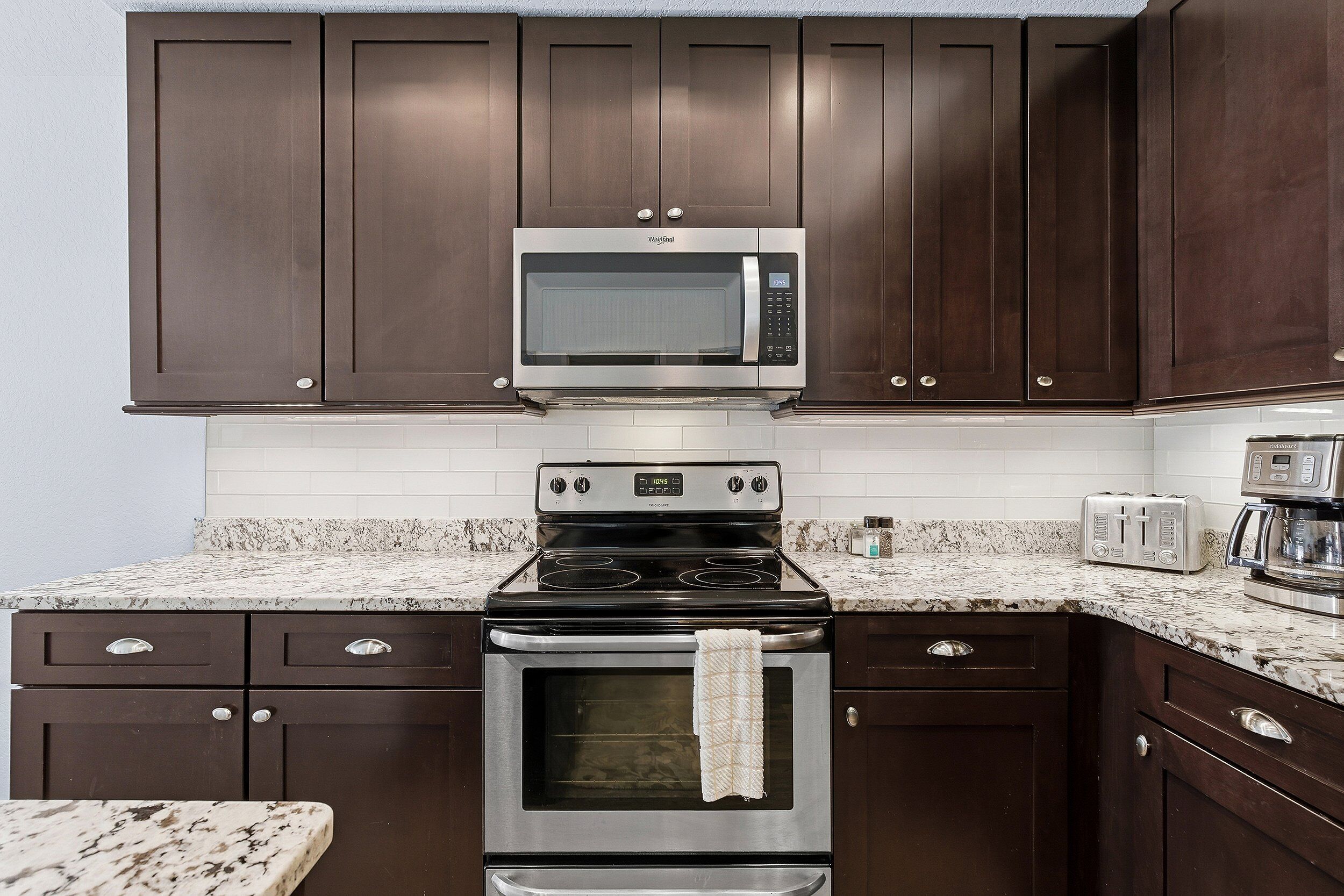 A kitchen with dark wooden cabinets, a stainless steel microwave, a black stove, and a granite countertop.